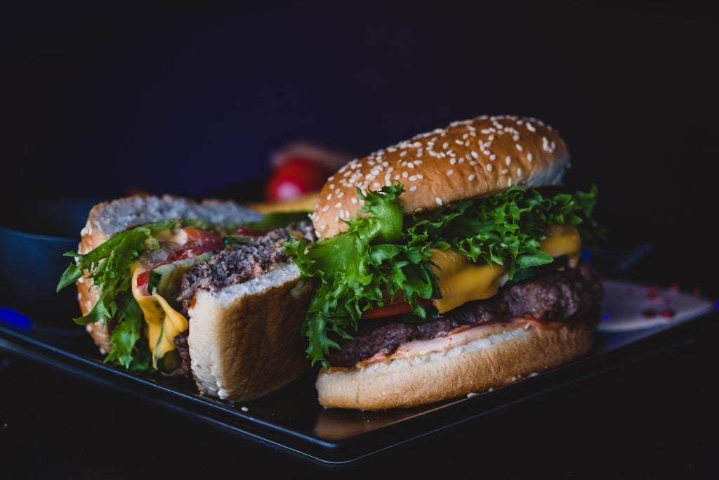 Up close shot of a delicious juicey thick burger with melted cheese and beautiful leafy greens on a sesame bun.