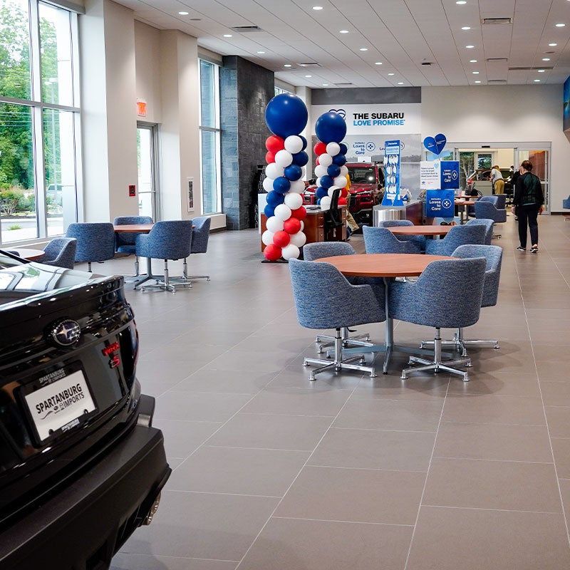 The lobby of Subaru of Spartanburg is pictured, showcasing tables and chairs, new Subarus, and a welcoming atmosphere