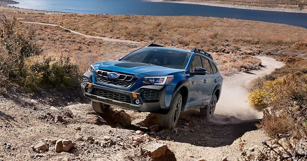2025 Subaru Outback in geyser blue driving uphill on an off-road trail.
