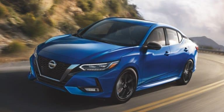 A blue Nissan Sentra drives down a winding road.