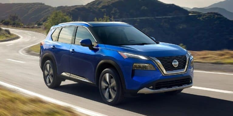 A blue 2021 Nissan Rogue drives down a country road