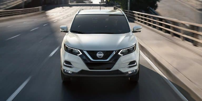 Front view of a white 2021 Nissan Rogue Sport driving over an overpass.