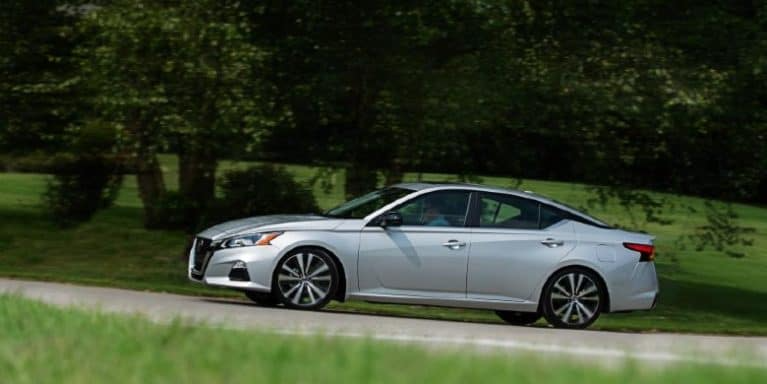 A silver Nissan Altima is parked near a grassy hill