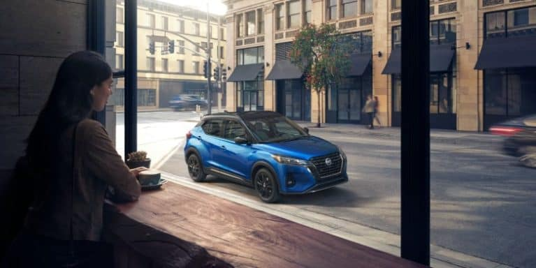 A woman looks out a coffee shop window at a blue 2021 Nissan kicks.