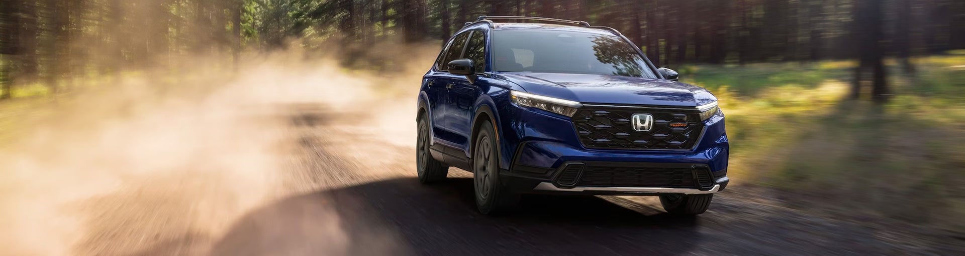 A blue Honda CR-V Hybrid TrailSport leaving a trail of dust driving on a dirt road.