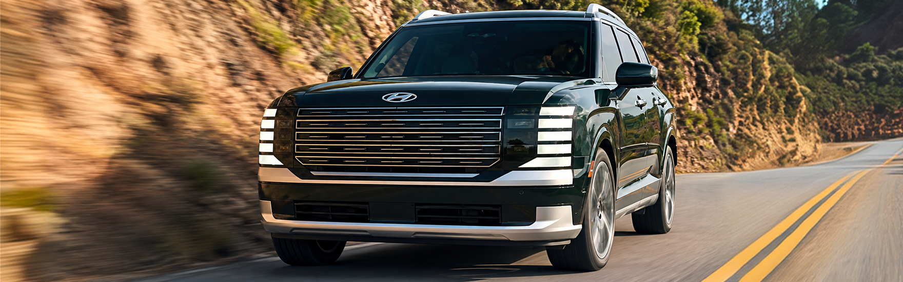 A dark green 2027 Hyundai Palisade driving along a winding mountain road