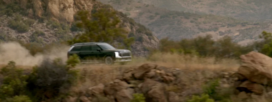 A Hyundai Palisade kicking up dust on a rugged dirt trail in the hills