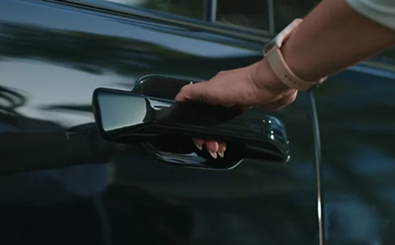 A hand opening the flush door handle of a dark green Hyundai Palisade