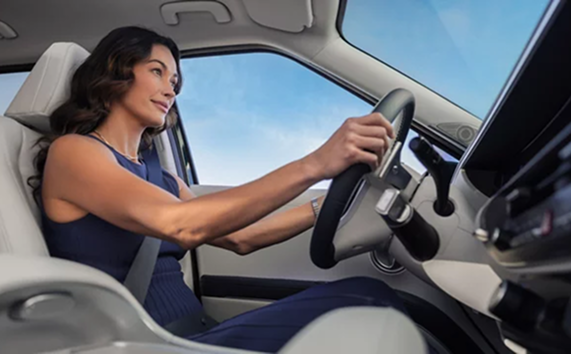A smiling woman driving a Hyundai Palisade with a light gray interior