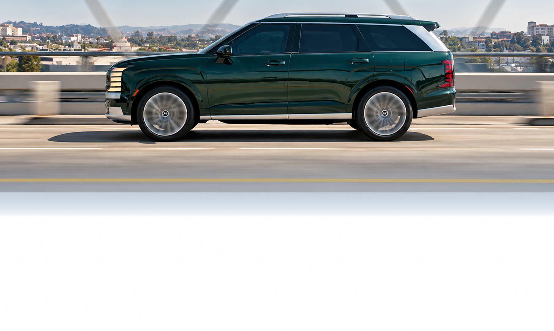 Side view of a dark green Hyundai Palisade driving across a city bridge