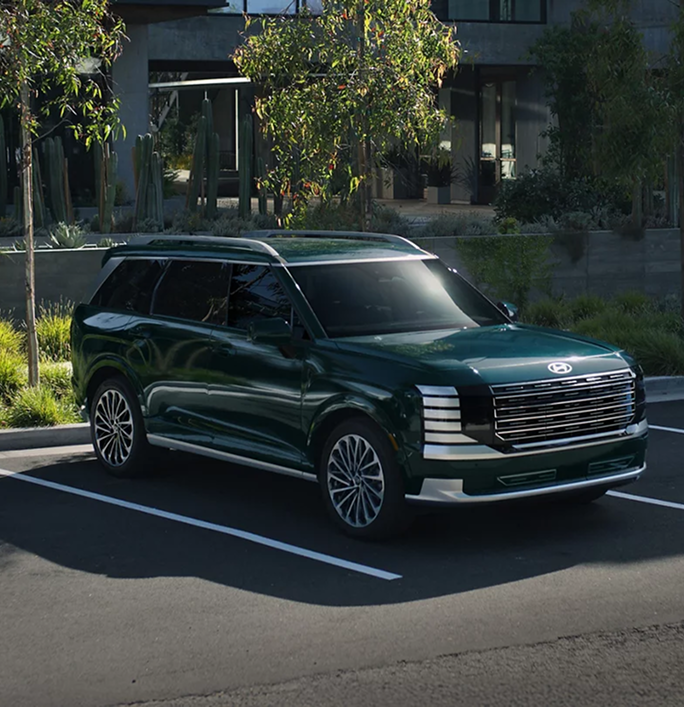 A dark green Hyundai Palisade parked in a lot lined with trees