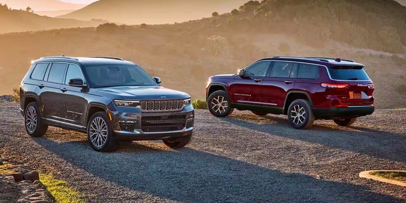 Two Jeep Grand Cherokees in different colors and trim levels - one red, one gray - sitting in a desert environment.
