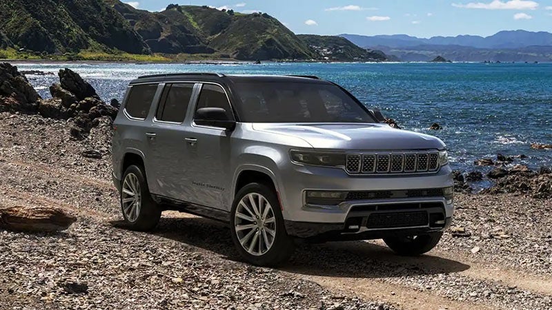 A silver Jeep Grand Wagoneer sitting on a rocky beach