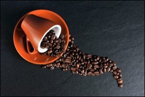 Coffee cup with beans pouring out on a plate and table