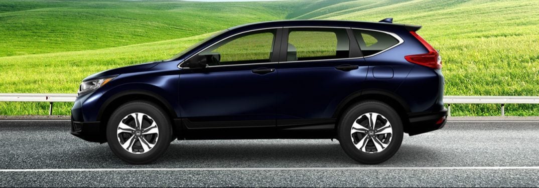 Purplish black 2019 Honda CR-V on a highway against a green field background, viewed from the side. It may or may not be bigger than past models.