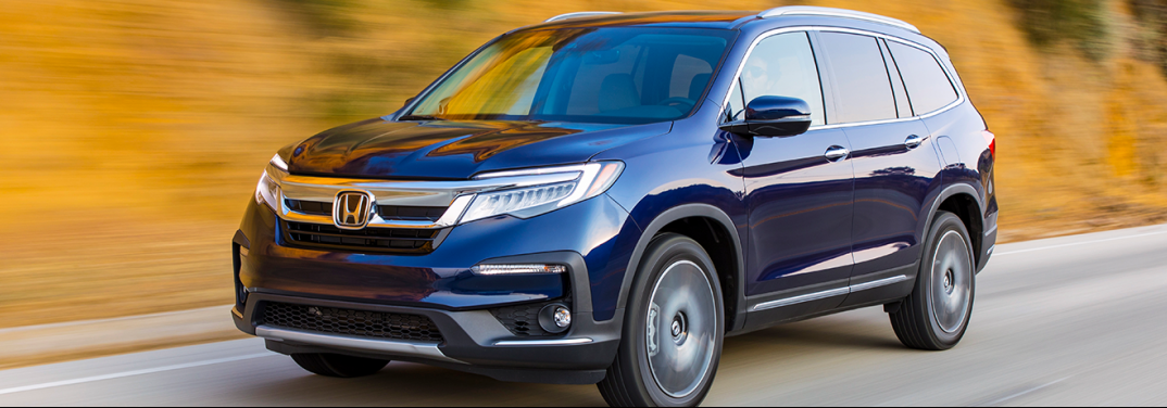 Blue 2019 Honda Pilot drives down a highway beside a yellow mound.
