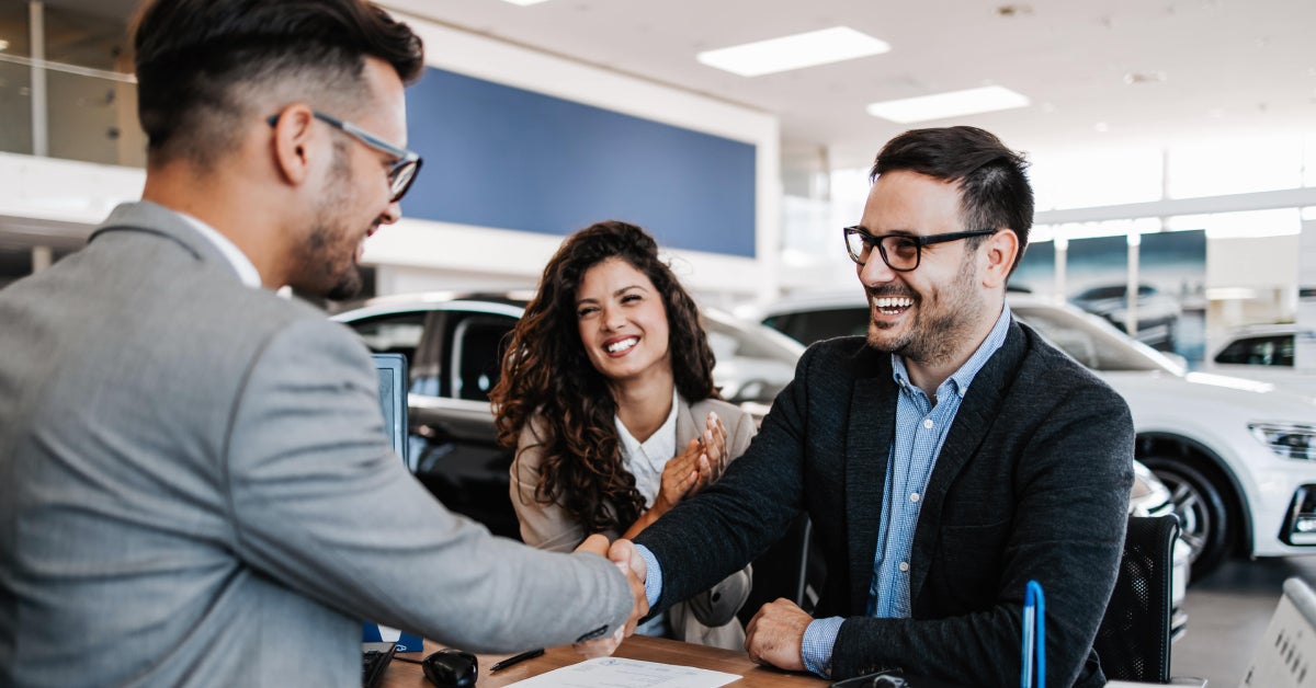 a couple making a deal with a car salesman in a car dealership