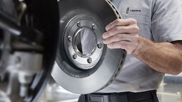 Lincoln technician fitting a new brake rotor onto the wheel hub Lincoln technician fitting a new brake rotor onto the wheel hub