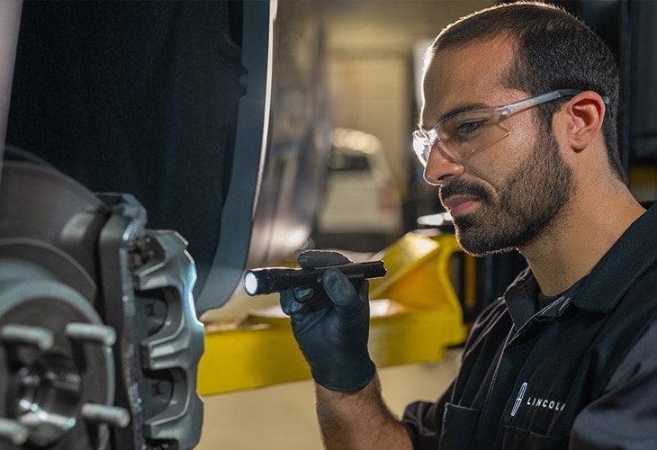 Lincoln technician in safety glasses inspecting a brake rotor and caliper with a flashlight Lincoln technician in safety glasses inspecting a brake rotor and caliper with a flashlight