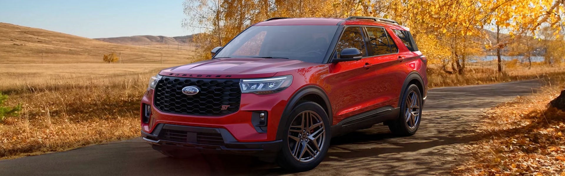 A red Ford Explorer SUV parked on a road surrounded by autumn trees.