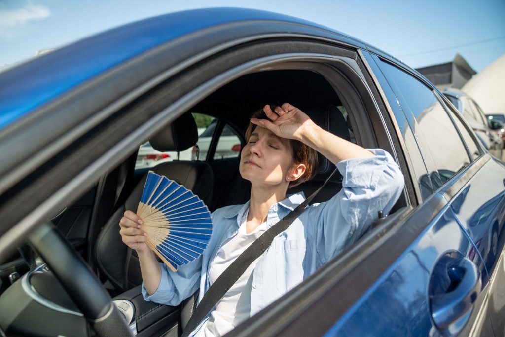 A woman fanning herself off in a hot car. 