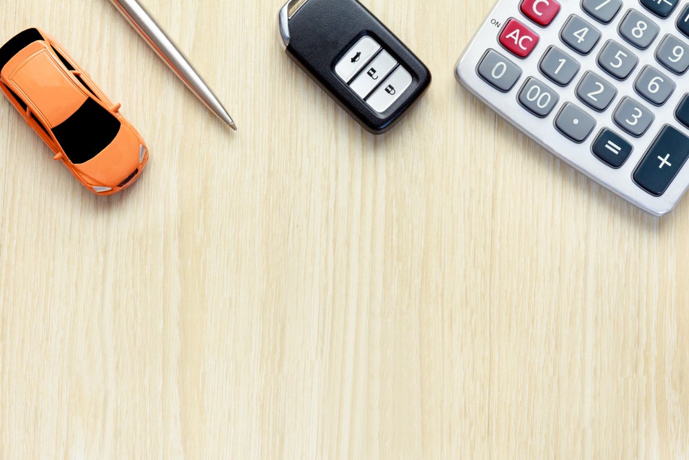 A wood surface with a toy car, car keys, pen, and calculator