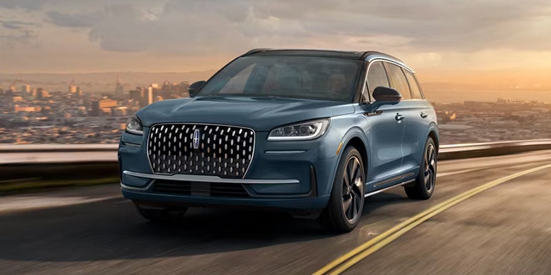 Blue Lincoln SUV driving on a highway with a city skyline in the background.