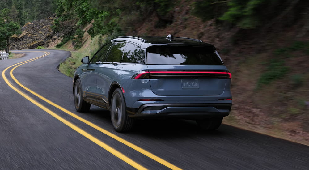 Rear of a blue 2026 Lincoln Nautilus driving around a bend.