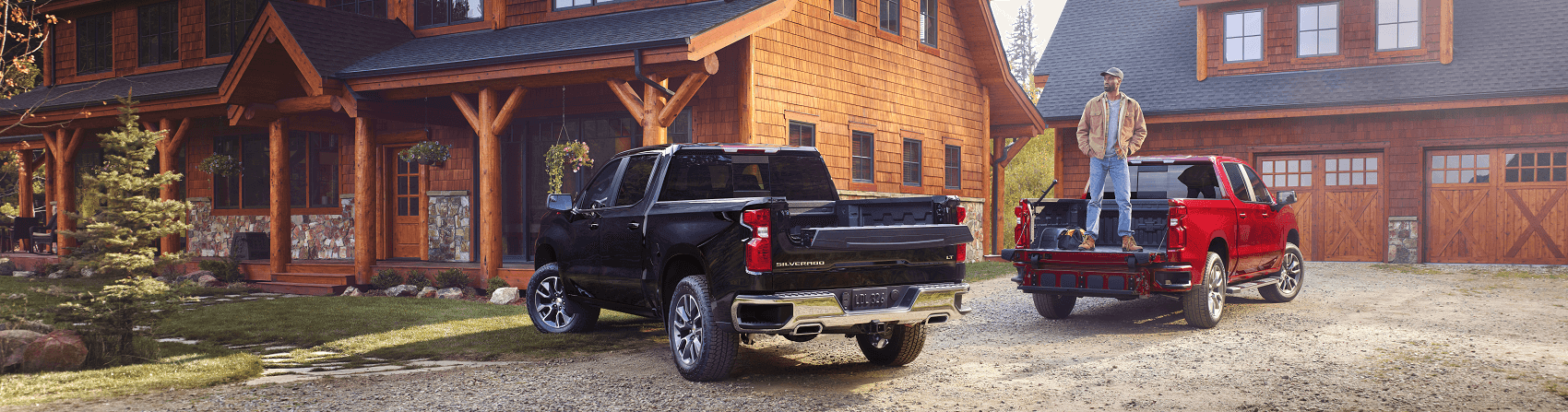 Man standing in bed of red Chevy Silverado 1500 next to black Silverado 1500