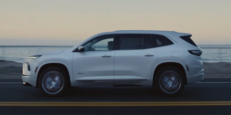 White Buick Enclave SUV driving along a coastal highway.