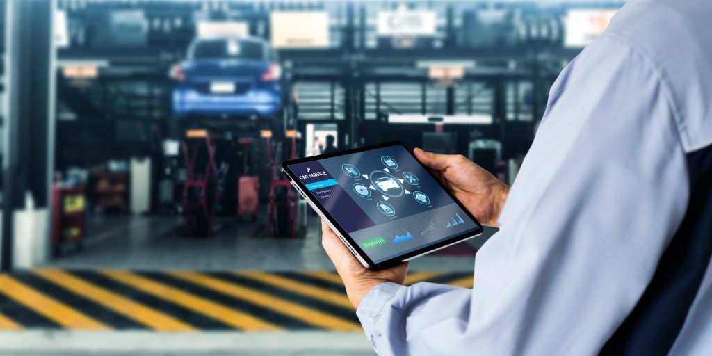 A technician using a tablet to access car service diagnostics in a garage.