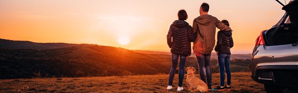 Family and dog watching a sunset on a road trip.