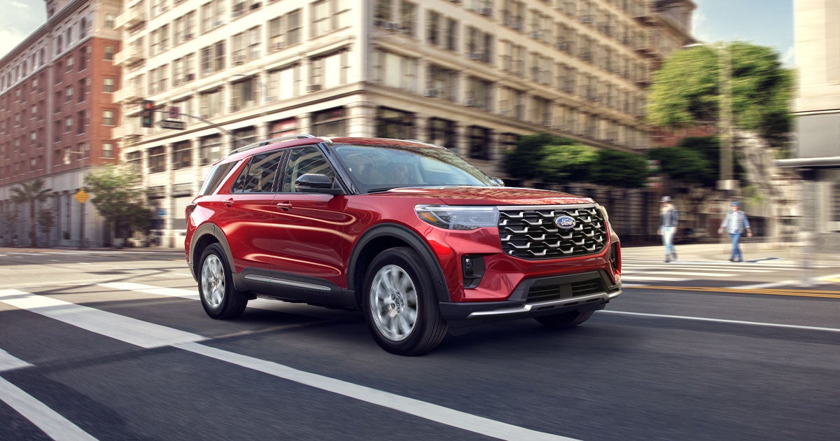 A red Ford Explorer on the road driving in a city.