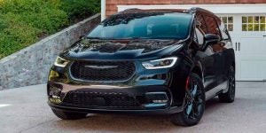 A black 2023 Chrysler Pacifica parked in a driveway, showcasing its sleek and modern design with a bold front grille and sporty accents.