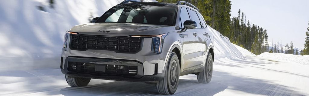 Silver Kia Sorento SUV driving on a snowy mountain road.