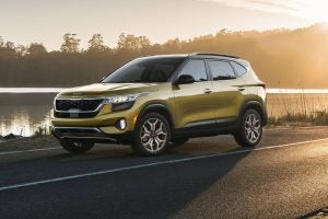 A yellow 2022 Kia Seltos on the backroads with the lake and trees in the background.