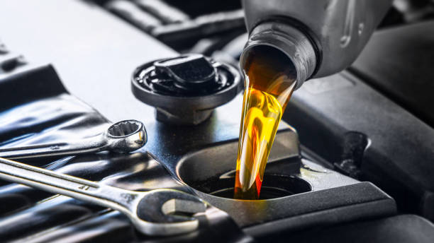 A close-up of engine oil being poured into a car's engine, with tools visible nearby.

