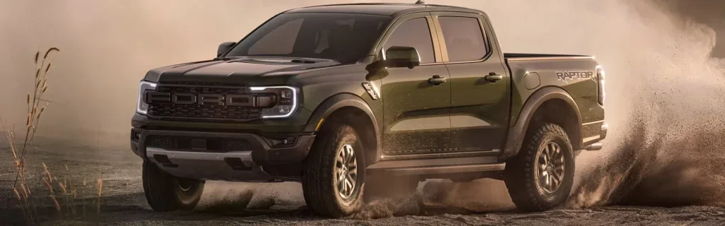 Ford Raptor pickup truck drifting off-road and kicking up dust.