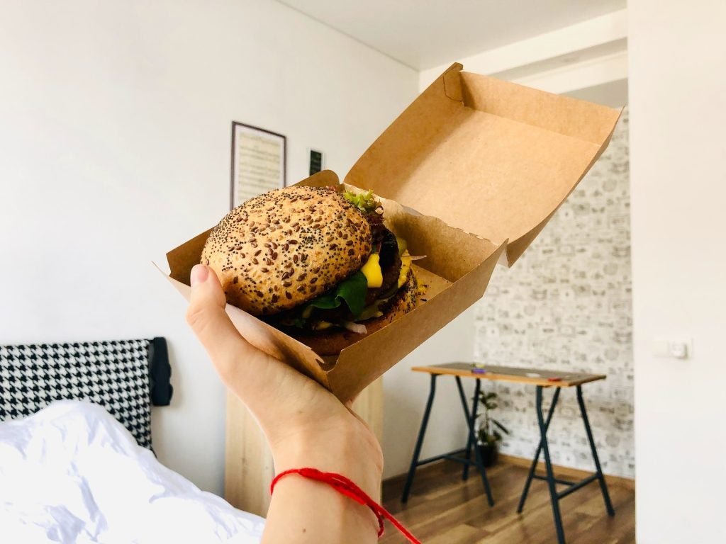 A hand holding a vegan burger in its take-out casing.