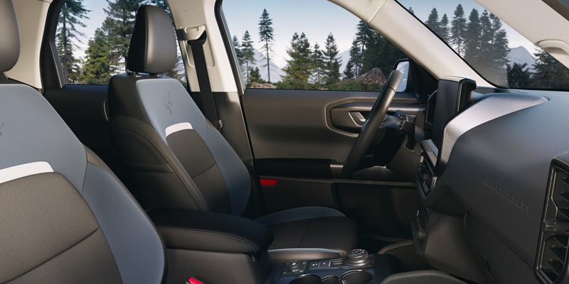 A close-up of the interior of a Ford Bronco SUV, showcasing the front seats, dashboard, and scenic outdoor view through the windows.