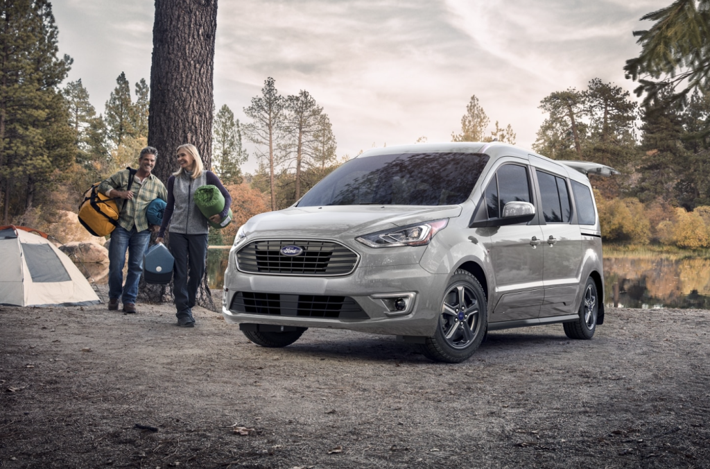 Two people unpacking their silver 2022 Ford Transit Connect to set up their camping site.