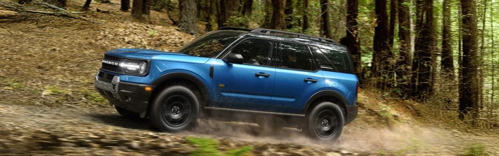 Blue Ford Bronco SUV driving through a forest trail off-road
