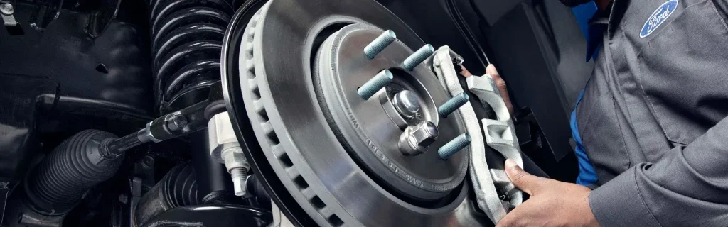 Close-up of automotive brake rotor and caliper being serviced by technician.
