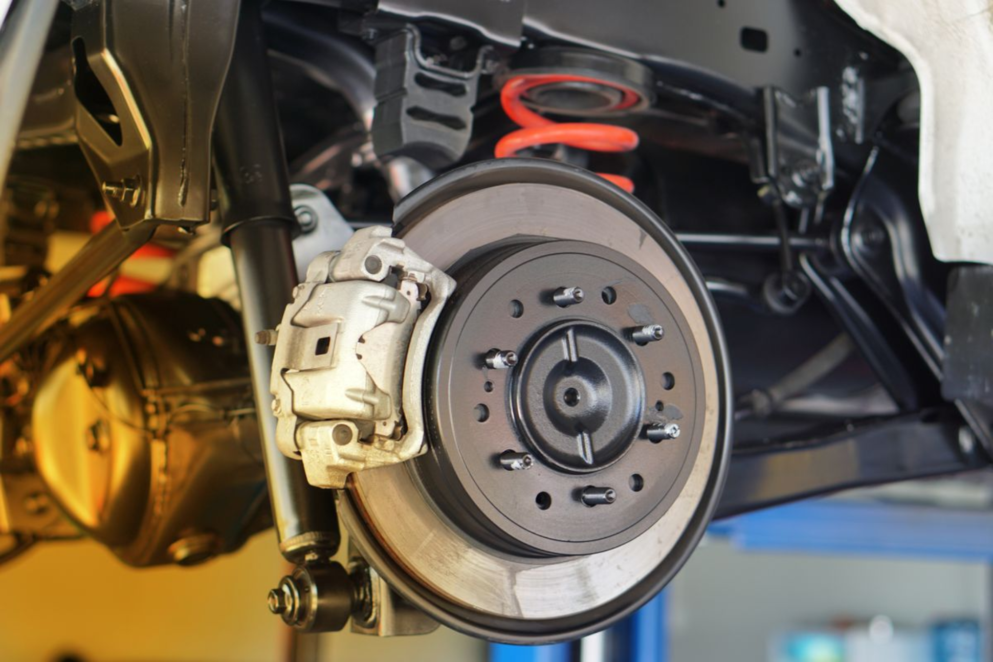 Close-up of a vehicle brake assembly showing rotor, caliper, and suspension components.