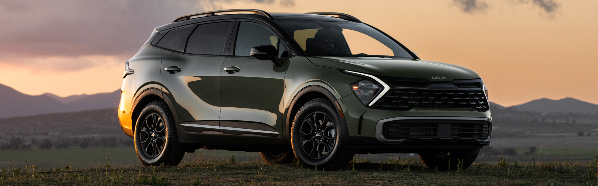 Front passengers side view of a green 2025 Kia Sportage parked on a field at dusk
