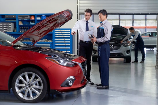 two men stand next to each other and look at the engine of a red car 