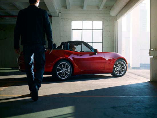 a man walks towards a red sportscar thats parked in a garage and has a woman sitting in it 
