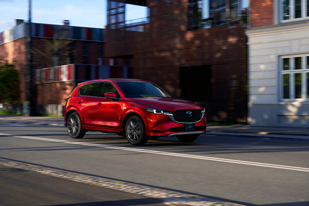 Red 2025 Mazda CX-5 SUV driving down a city street