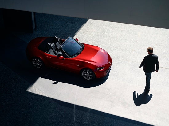 an overhead shot of a man walking towards a red miata 