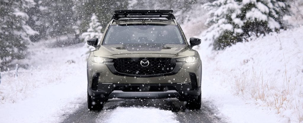 a grey mazda awd facing towards the camera driving through the snow